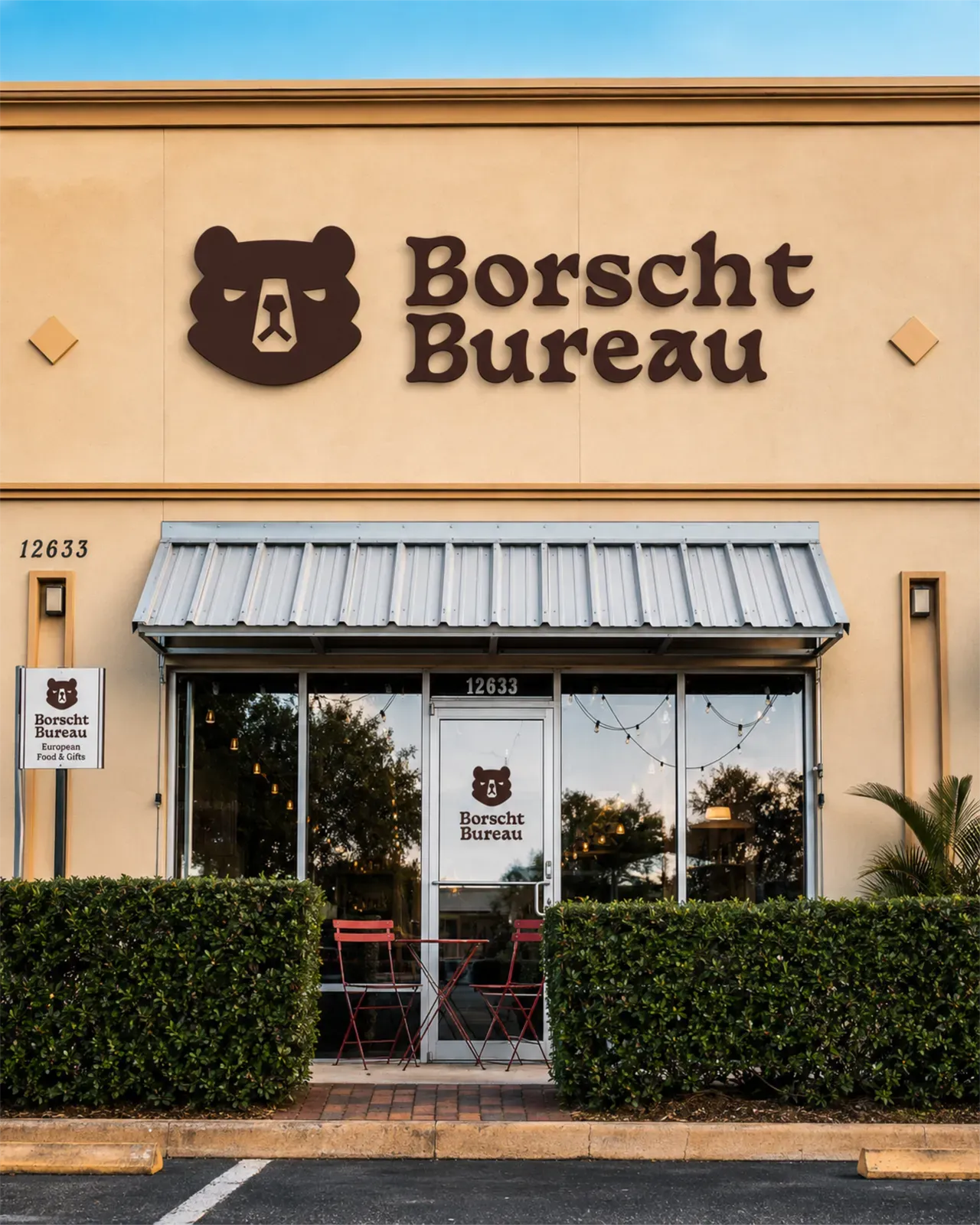 The Borscht Bureau storefront at dusk — bear mark and wordmark mounted above the awning, café tables by the door.